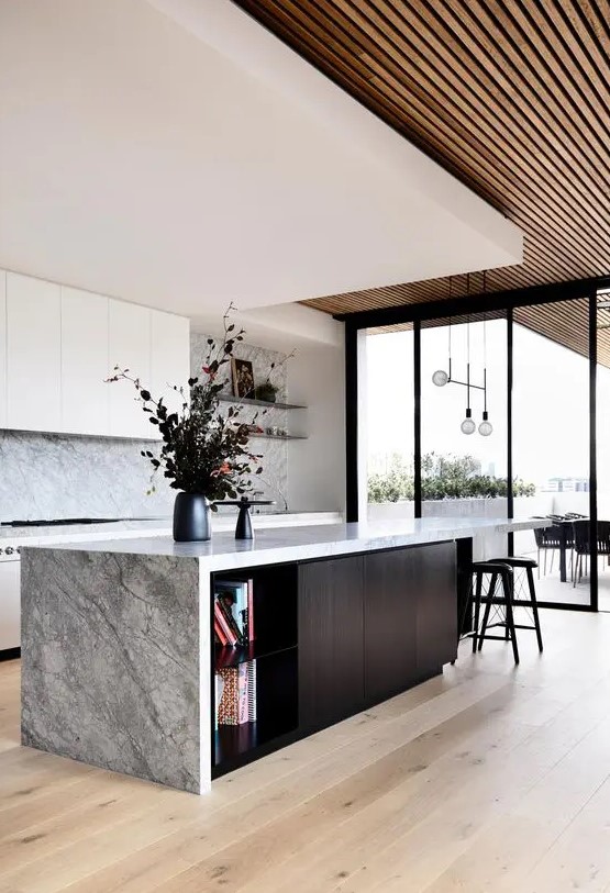a gorgeous contemporary ktichen with sleek white cabinets, a grey stone backsplash and countertops, a black kitchen island and a layered ceiling