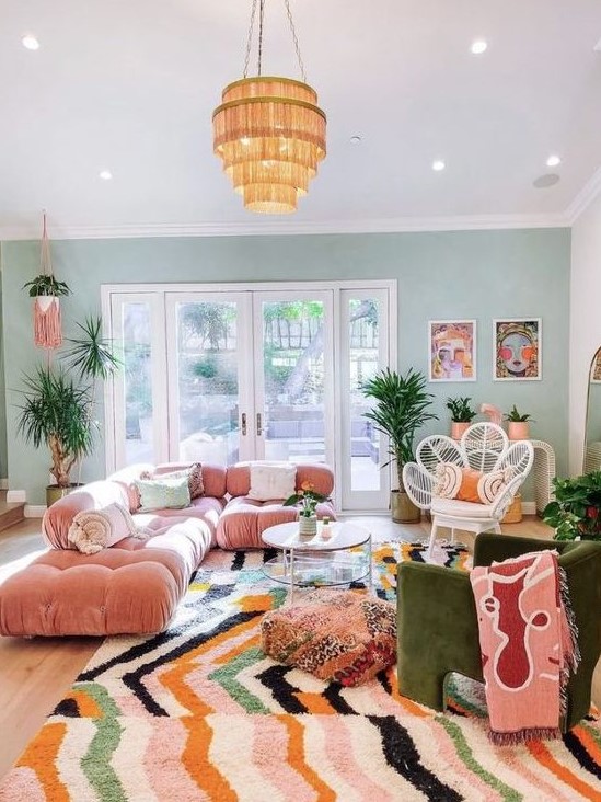 a maximalist living room with a green accent wall, a pink sofa, a green chair, a bright rug and a glazed tiered table