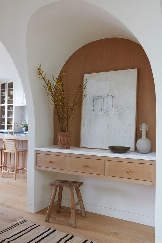 an arched niche with a built-in desk with drawers, vases and art plus a small stool is enough for doing some stuff