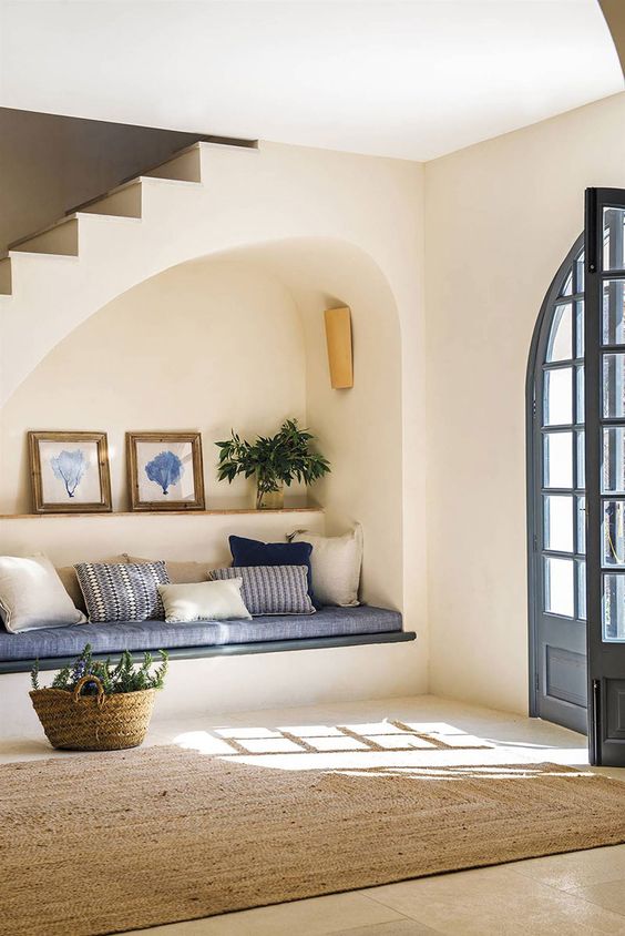 an arched niche with a built in sofa with pillows, a shelf with art and greenery plus a lamp is a cool solution for an entryway