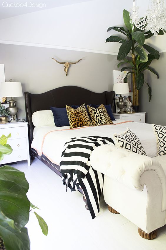 a catchy neutral bedroom with a black upholstered bed, mixed print bedding and pillows, potted plants and an upholstered bench
