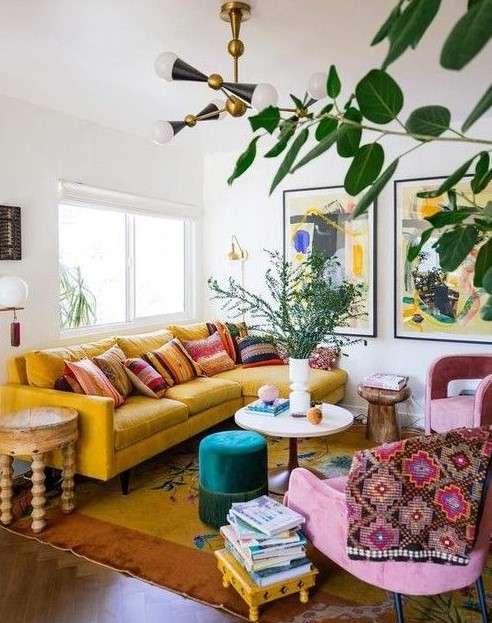 a maximalist living room with a yellow sofa, pink chairs, various tables and bold artworks plus potted plants