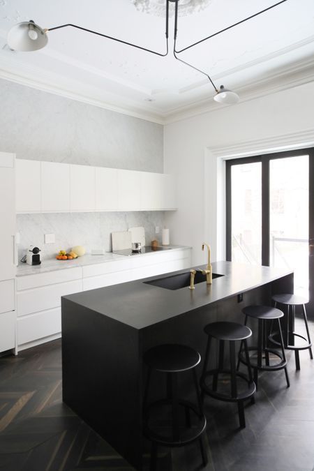 a minimalist white kitchen with sleek cabinets, a black kitchen island, black stools and gold touches