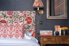 41 a moody bedroom with black grasscloth wallpaper, a bold floral headboard and printed pillows, a printed sconce and a stained nightstand