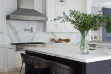 42 a modern farmhouse kitchen with white shaker style cabinets, a large metal hood, a black kitchen island, a white marble backsplash and countertops