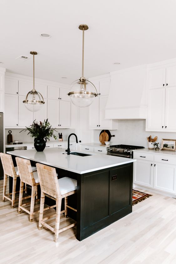 a modern white farmhouse kitchen with shaker cabinets, a black kitchen island, white woven stools and sphere pendant lamps