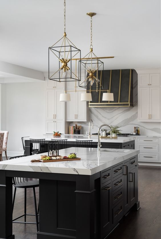 a refined white kitchen with shaker cabinets, a large black kitchen island, a hood with gold touches and pendant lamps over the island