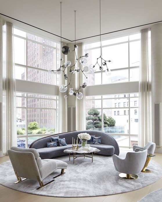 an elegant double-height living room with a curved blue sofa and matching chairs plus gold touches here and there