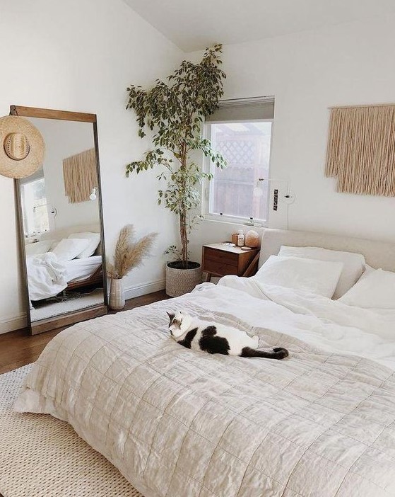 a neutral boho bedrom with a statement potted plant in the corner that makes it fresher and more welcoming