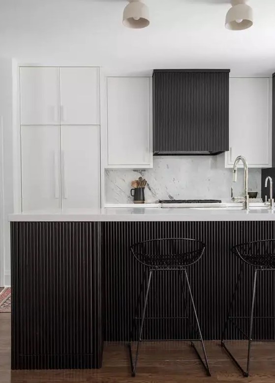 an elegant and laconic black and white kitchen with white and black reeded cabinets and a matching kitchen island plus black stools