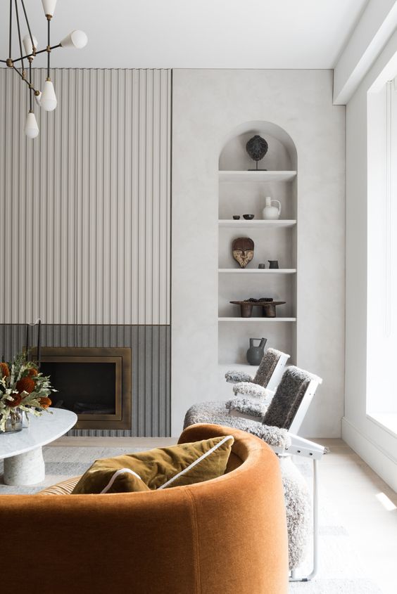 a contemporary living room with a fluted detail, an arched niche, grey chairs and a rust one, a coffee table
