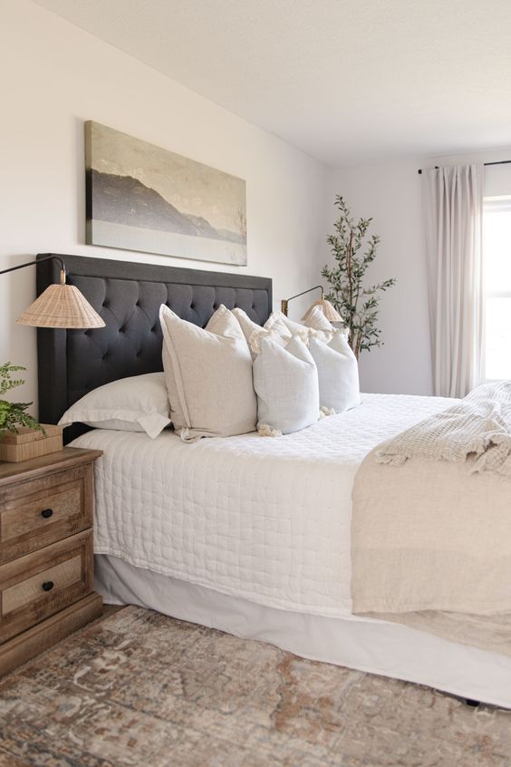 a soothing neutral bedroom with a charcoal grey upholstered bed, neutral bedding, a stained wooden nightstand