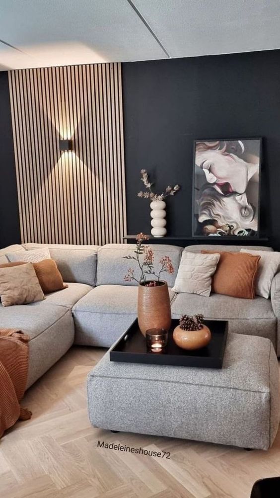 a living room with black walls. a fluted detail, a low grey sofa and a matching ottoman, rust decor