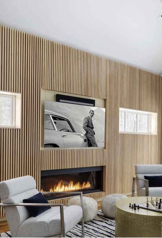 a neutral contemporary living room with a fluted wooden wall, a built-in fireplace, a TV and neutral chairs