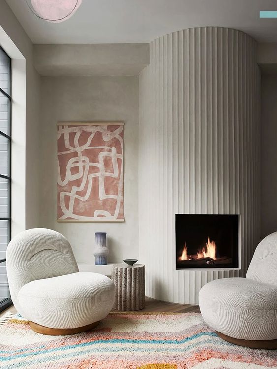 a neutral living room with a white fluted fireplace, creamy chairs, a bold printed rug and a bold artwork