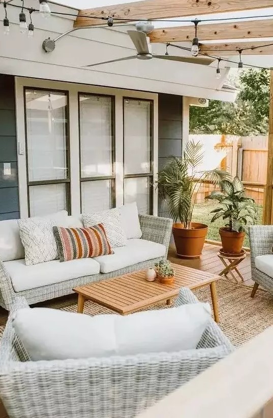 a cool modern outdoor living room with neutral woven furniture, printed pillows, a wooden table and potted plants welcomes