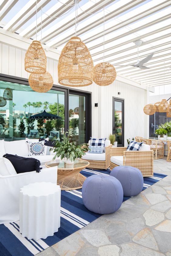a coastal living room with a white sofa, woven chairs, a rattan table, a bold blue rug and blue poufs