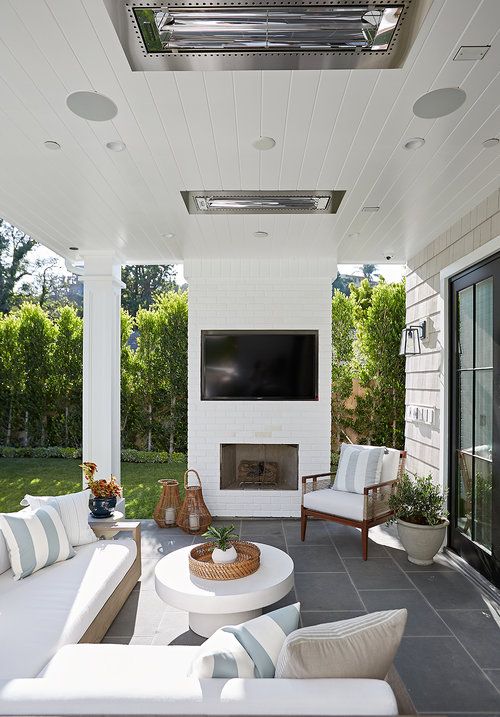 a neutral outdoor living room with a built-in fireplace, a neutral sofa and chairs, a white round coffee table and woven lanterns