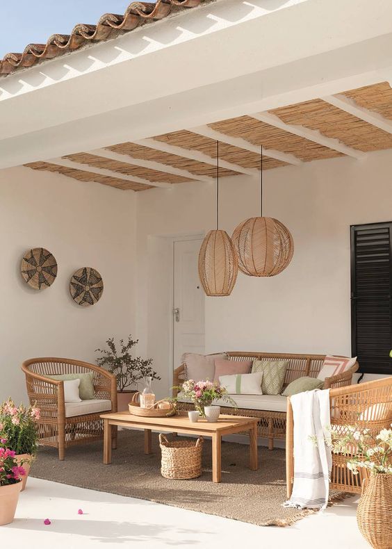 a beautiful outdoor living room with a woven sofa and chairs, a wooden table, printed pillows and woven pendant lamps