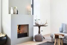 a Scandinavian space with a concrete fireplace with a mantel, a grey sofa, stools and a grey rug, pillows and a table with decor