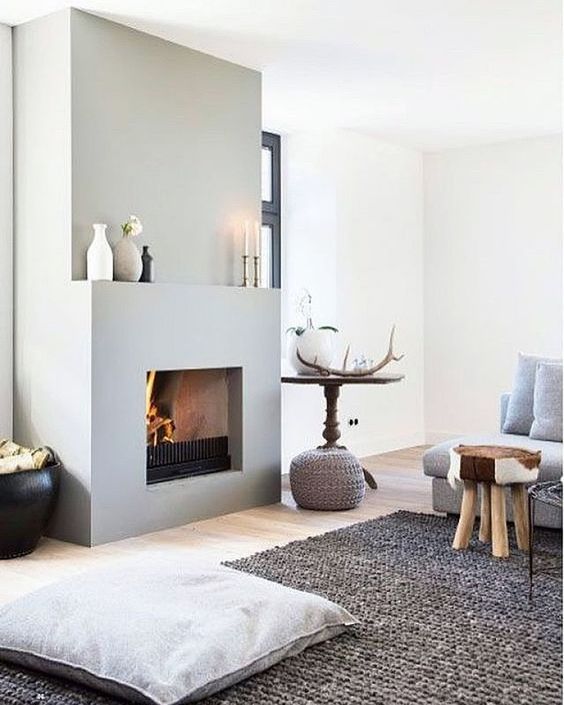 a Scandinavian space with a concrete fireplace with a mantel, a grey sofa, stools and a grey rug, pillows and a table with decor