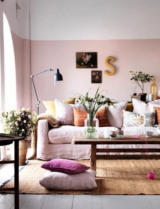 a beautiful and relaxed feminine living room with color block walls with pink, a pink sofa with colorful and printed pillows, artworks, blooms and greenery and a rust-colored rug