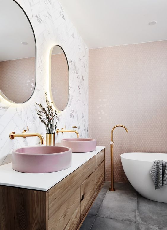 a beautiful bathroom with a marble herringbone tile wall and a pink penny one, a concrete floor and a floating vanity with pink sinks