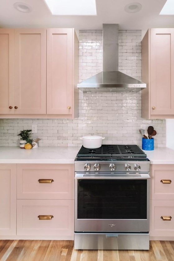 a beautiful blush kitchen with brass handles, a white tile backsplash and skylights is very tender and delicate