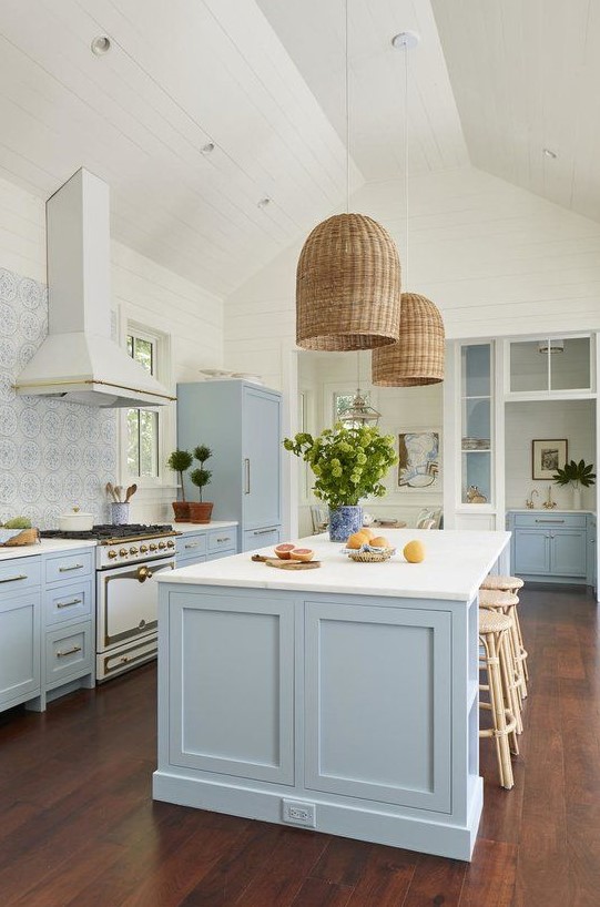 a beautiful coastal kitchen in light blue and white, with a mosaic tile backsplash, wicker lampshades and rattan stools plus greenery