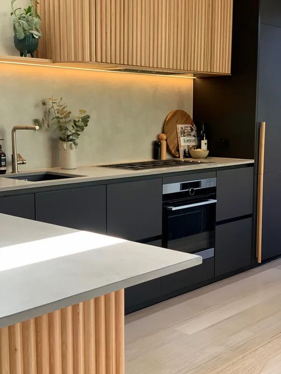 a beautiful contemporary kitchen with matte black cabinets and a fluted hood, a fluted lower cabinet and built in lights