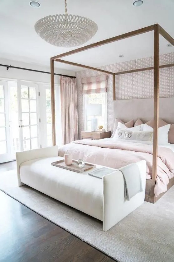 a beautiful feminine bedroom with a wallpaper accent wall, a canopy bed, blush bedding and curtains and a chic chandelier