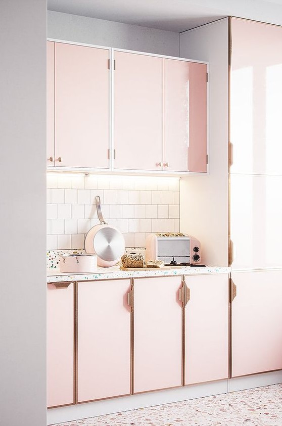 a beautiful light pink kitchen with chic brass handles, a white tile backsplash and a terrazzo floor and backsplash