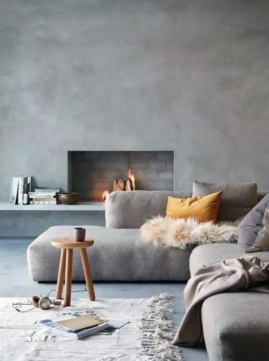 a beautiful minimalist living room with chic furniture, a concrete wall and a fireplace and cozy textiles
