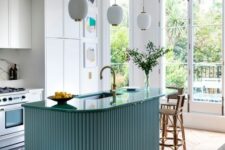 a beautiful modern kitchen with white cabinets, a blue fluted and curved kitchen island, pendant lamps and an eating zone
