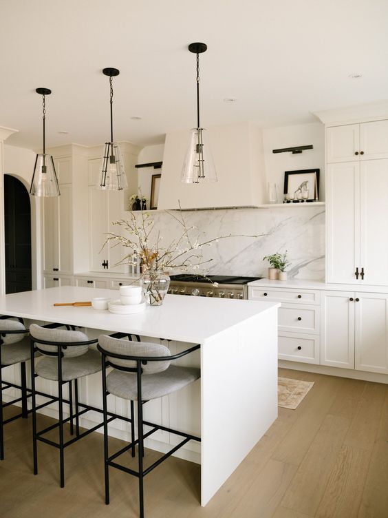 a beautiful modern kitchen with white shaker cabinets, a white quartz backsplash, a white kitchen island and glass pendant lamps