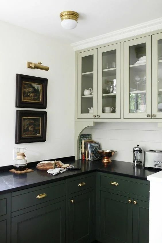 a beautiful two-tone green kitchen with a beadboard backsplash, black marble countertops and vintage artwork