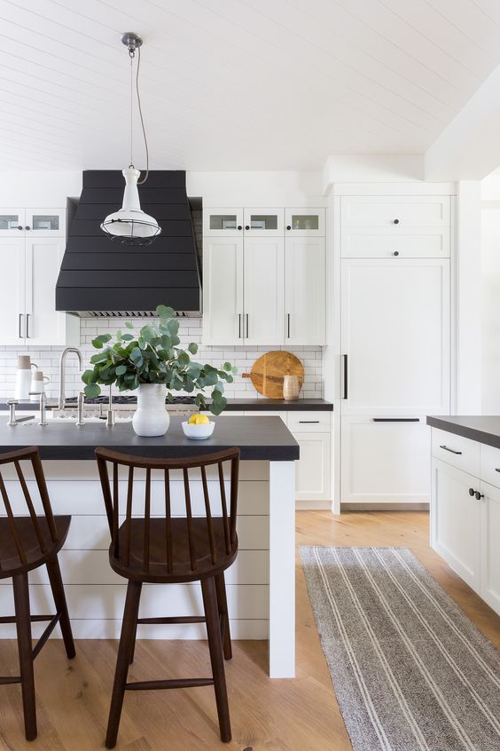 a black and white farmhouse kitchen with white shaker cabinets, black countertops, white tiles on the backsplash and stained stools