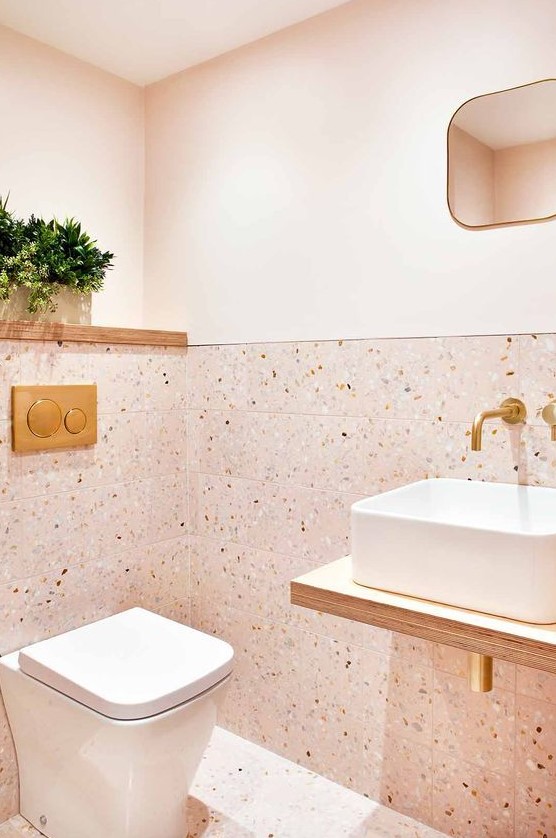a blush powder room with terrazzo tiles and paint, a floating vanity and gold fixtures and touches here and there