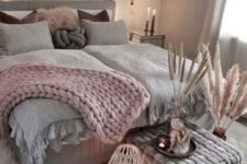 a boho Scandi bedroom with grey walls, a grey bed with pink and grey bedding, a grey pouf, a white rug, pampas grass and candles