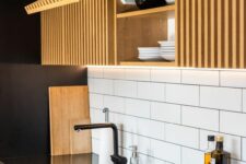 a bold and contrasting kitchen with sleek black surfaces that are juxtaposed to light-stained ribbed cabinets