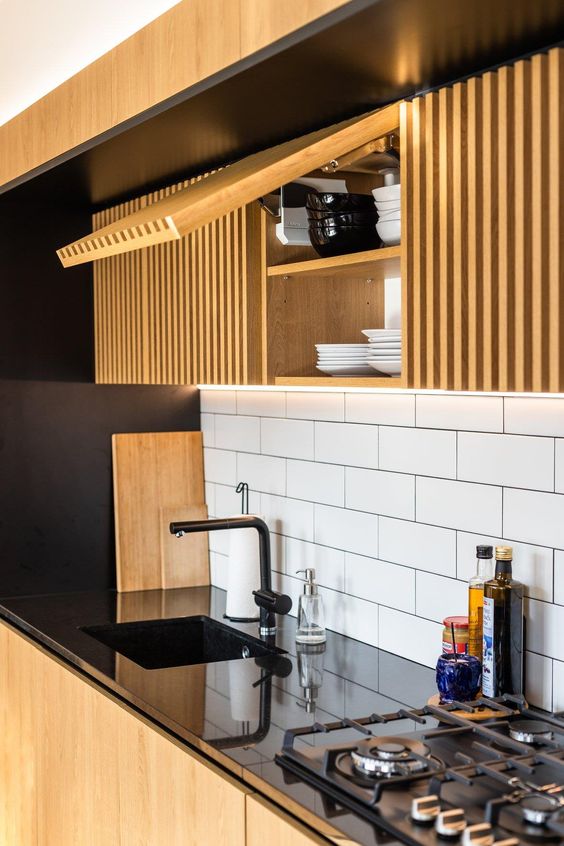 a bold and contrasting kitchen with sleek black surfaces that are juxtaposed to light stained ribbed cabinets