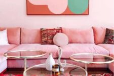a bright and feminine living room with light pink walls, a pink sofa, a glass coffee table, a bold artwork and a colorful rug with prints