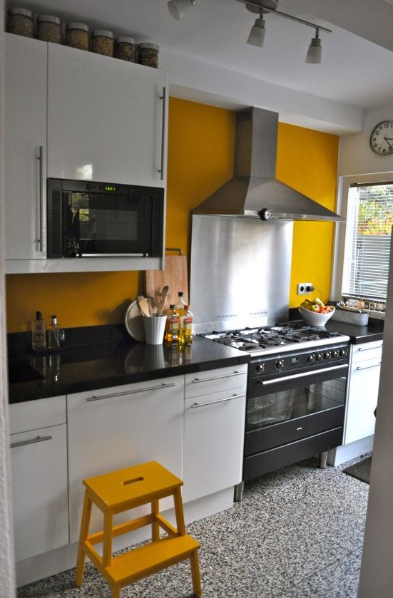 a bright kitchen with a mustard wall and a stool and black and white everything to calm that down a bit