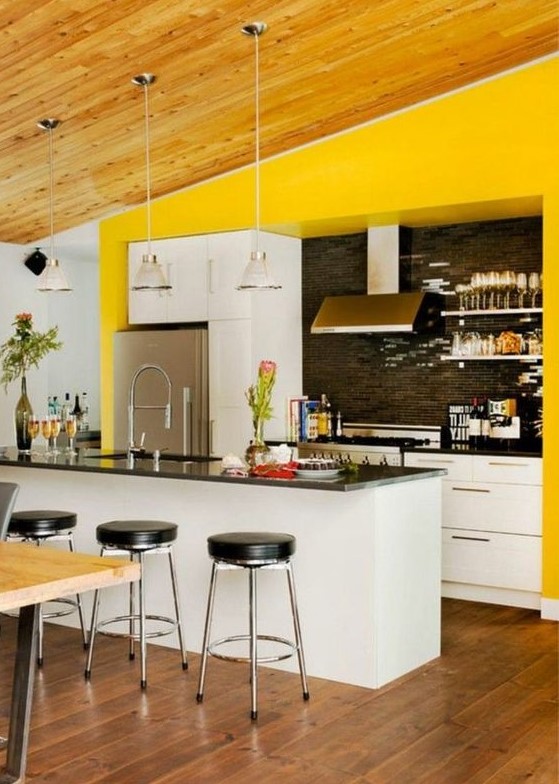 a bright kitchen with white cabinetry, black countertops and a backsplash, black stools and white lamps