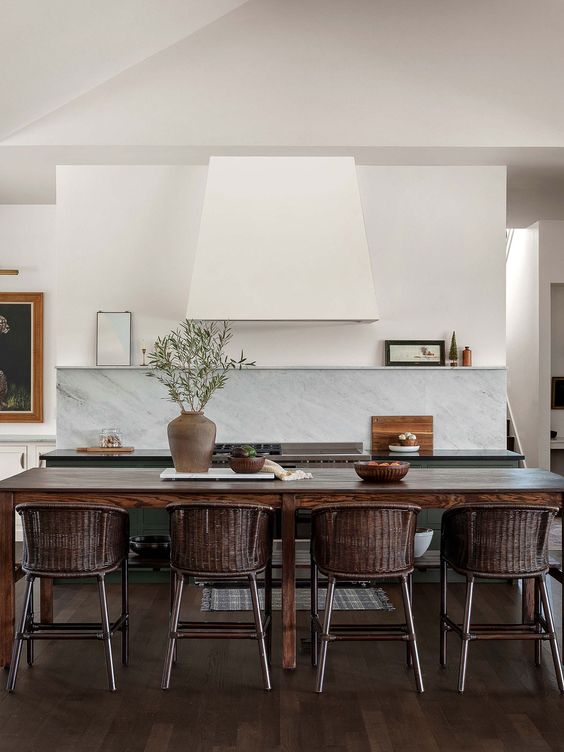 a catchy kitchen with green cabinets, a white hood and a shelf, a stained table and chairs, a white quartz backsplash