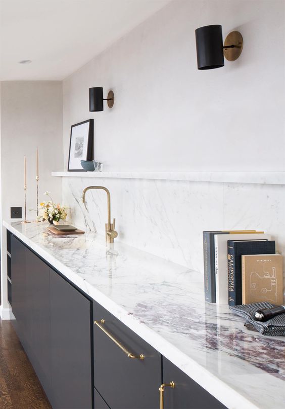 a charcoal grey kitchen with a white quartz backsplash and countertops plus gold fixtures and black spotlights
