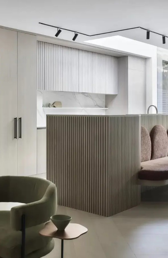 a chic contemporary kitchen in white, with sleek and fluted cabinetry, a marble countertop, a fluted grey kitchen island and spotlights