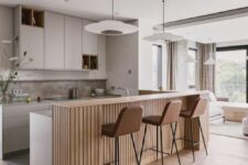 a chic contemporary kitchen with sleek grey cabinets with niches for storage, a double height kitchen island with a fluted part