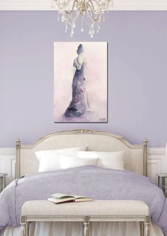 a chic feminine bedroom in lilac and neitrals, with lilac walls, neutral refined furniture, lilac bedding and an artwork plus a crystal chandelier