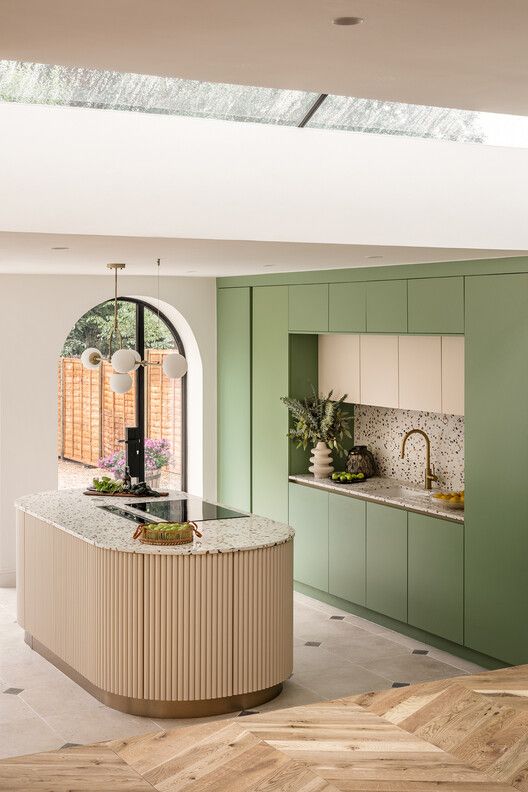 a chic modern kitchen with sleek green cabinets, a terrazzo backsplash and countertops and a curved kitchen island